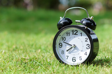 Wall Mural - A classic black alarm clock resting on green grass, signifying time and nature.