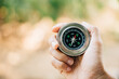 © sorapop - A traveler holding a compass in a park seeks guidance and direction. The compass in a woman hand set against a nature-blurred background signifies exploration and a journey to find one way.