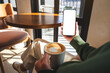 © Farknot Architect - Mockup image of a woman holding mobile phone with blank desktop screen while drinking coffee in cafe