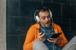 © tetxu - middle aged man with headphones and surprised gesture sitting on the street using digital tablet