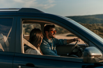 Young couple on a road trip, savoring the beauty of a sunset from their car