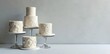 © Mali - Elegant white cakes adorned with intricate lace designs, displayed on glass cake stands against a neutral backdrop.