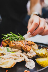 Wall Mural - A close-up of a gourmet dish featuring grilled chicken served on a plate with creamy sauce, garnished with fresh herbs, and accompanied by pickles and vegetables.