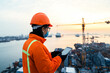© Александра Ходорковс - Asian male young worker in safety gear overseeing port operations at sunset
