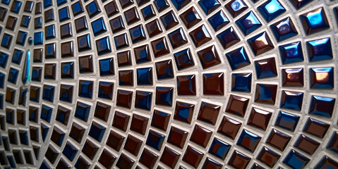 Poster -  A close-up of a wall consisting of small square tiles. The tiles are arranged in a grid pattern, each tile has a different color - blue, brown and silver. 