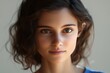 © Veronika - Young woman with curly hair gazing directly into the camera with a serene expression, showcasing natural beauty and warm lighting indoors