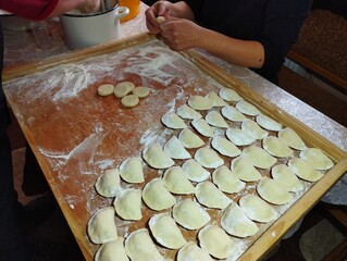 Woman manually makes varenyki. In the photo, female hands are molding varenyki. Raw varenyki are laid out on a wooden board. Cooking theme.