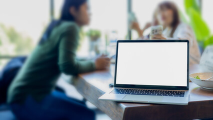 Poster - Laptop with blank screen placed on sugar wooden table in blurred people in blurred business meeting background, laptops on desk in workspace coffee cafe blur team discussion background.