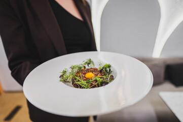 Wall Mural - A gourmet dish featuring a delicate blend of ingredients, topped with a bright egg yolk, garnished with fresh greens, served in an elegant white plate. Perfect for culinary presentations.