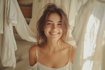 Wall Mural - Smiling young woman with long hair, sitting amidst softly draped fabric, radiating warmth and joy in a cozy, bright environment.