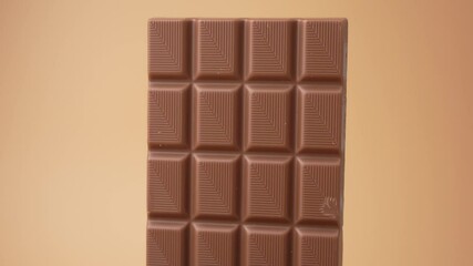 Wall Mural - Chocolate rotates on an orange background. The chocolate bar is cut into squares. The squares don't touch each other