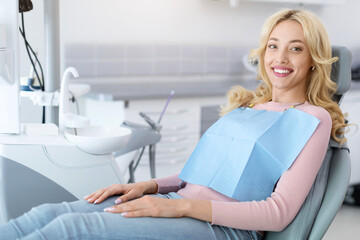 Side view of pretty blonde young woman patient sitting in dental chair and smiling, copy space. Cheerful millennial lady showing beautiful white smile after treatment at modern dental clinic