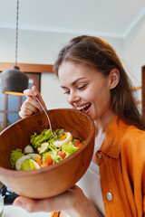 Canvas Print - Young woman enjoying a fresh salad in a wooden bowl, smiling with joy in a cozy kitchen setting, showcasing healthy eating and vibrant colors