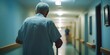 © Kartika - A man in a white shirt and blue pants is walking down a hallway with a cane