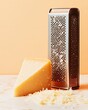 © Dai - Parmesan cheese block with a fine grater and a sprinkling of shavings, placed on a marble countertop, isolated on a pale orange background