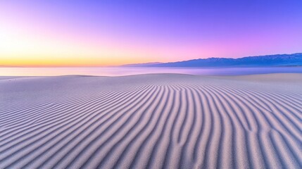 Wall Mural - Serene desert landscape at dawn, with rippled sand dunes meeting a hazy horizon. Sunrise colors paint the sky in a blend of pinks, purples, and golds, reflecting on the tranquil water.