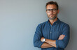 © muhammadarslan - Confident stylish man with short hair and beard, wearing glasses and a blue shirt, arms crossed, isolated on white background, casual outfit, professional photo shoot pose