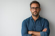 © muhammadarslan - Confident stylish man with short hair and beard, wearing glasses and a blue shirt, arms crossed, isolated on white background, casual outfit, professional photo shoot pose