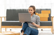 © Nittaya - Startup Success: A young woman, the founder of her own online business, works diligently on her laptop, surrounded by boxes ready for shipment. The image captures the spirit of entrepreneurship.