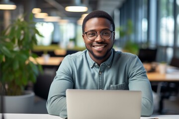 Poster - Portrait of a happy african american businessman working on a laptop in a modern office