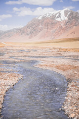 Wall Mural - High-mountain river flows in a valley against the background of rocky mountain ranges in the Tien Shan mountains in the Pamirs in Tajikistan, landscape for background