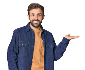 Wall Mural - Studio portrait of young Hispanic male showing a copy space on a palm and holding another hand on waist.