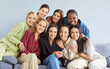 © Studio Romantic - Portrait of group of female happy cheerful young diverse women friends coworkers or company employees hugging and looking at camera posing and smiling sitting on sofa on gray background.