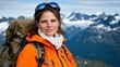 © Anna - woman stands confidently in a bright orange jacket and backpack, smiling against a breathtaking backdrop of snow-capped mountains on a clear, sunny day