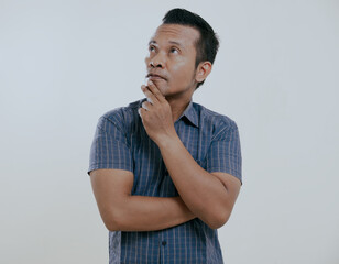 Wall Mural - Asian man showing thinking gesture with his eyes looking up isolated on white background.