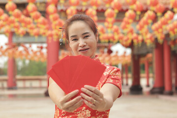 Wall Mural - Asian woman with red traditional cheongsam qipao dress holds red envelopes Ang Pao in Chinese building. Portrait of happy girl celebrating Chinese New Year. Chinese tradition festival holiday.