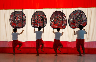 Wall Mural - Four player men stand with perform grand shadow play in front of white screen with lift leg as performance of the show.