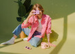 © Anna Tsukanova/Stocksy - Woman with film camera and pink denim coat on green background