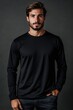 © Aleksander - A confident young man with a well-groomed beard, wearing a black long sleeve T-shirt mockup, standing against a dark background. He has a serious expression and is posing with one hand in his pocket.