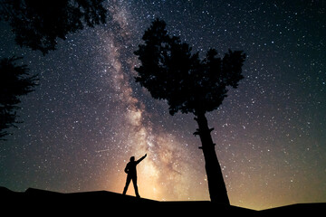 Wall Mural - Silhouette of a  hiker standing on the hill,  under milky way galaxy sky. Beautiful night landscape.