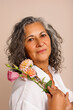 © valbar STUDIO/Stocksy - A woman with  gray hair holds a bouquet of flowers