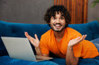 © ViDi Studio - Young amazed IT Indian man wear casual clothes lay on blue sofa couch hold use work on laptop pc computer stay at home hotel flat rest relax spend free spare time in living room indoor Lounge concept