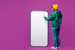 © ViDi Studio - Full body young Indian man in green hoody yellow hat casual clothes point index finger on big huge blank screen area mobile cell phone smartphone isolated on plain purple background Lifestyle concept