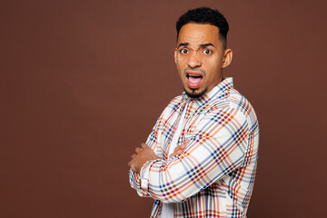 Wall Mural - Side view young sad mad man of African American ethnicity he wear blue shirt casual clothes hold hands crossed folded look camera isolated on plain brown background studio portrait. Lifestyle concept.