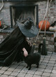 © Tana Teel/Stocksy - witch leans own to pet her black cat near outside fireplace