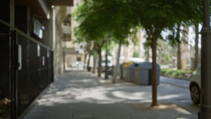 Wall Mural - Blurred outdoor scene on a city street with green trees, buildings, and bins, showcasing an urban setting with defocused shadows and light from a sunny day.