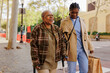 © BONNINSTUDIO/Stocksy - Caregiver walking with elderly woman using crutches in the city