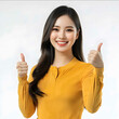 © estrel - Asian woman confident sunny smiling yellow long sleeves right hand thumbs up white background facing front