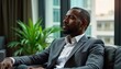 © Pete - Thoughtful African American executive relaxes in luxury condo office. Businessman sits comfortably on sofa looking out window. Stylish suit, pensive expression suggest moment of reflection. Modern