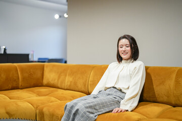 Wall Mural - A Japanese woman in her 30s is relaxing on the sofa in her living room.