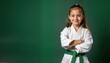 © Pete - Young girl in white martial arts uniform with green belt confidently poses with arms crossed. Demonstrates dedication to martial arts training. Studio portrait evokes determination, strength. Photo