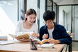 © bongkarn - Two young Asian college students are studying and preparing for an exam together in a coffee shop.