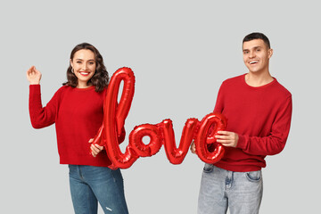 Canvas Print - Loving young couple with balloon in shape of word LOVE on grey background. Celebration of Saint Valentine's Day