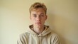 © AiPhotoSale - A contemplative young man with a faint frown gazes directly at the camera, set against a warm cream-colored backdrop with a light beige hoodie