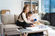 © Phushutter - Asian young mother and her daughter sit together on the sofa in the cozy living room, working on homework at the desk, creating a warm and supportive atmosphere for learning, love, hug, mother days.