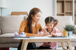 © Phushutter - Asian young mother and her daughter sit together on the sofa in the cozy living room, working on homework at the desk, creating a warm and supportive atmosphere for learning, love, hug, mother days.